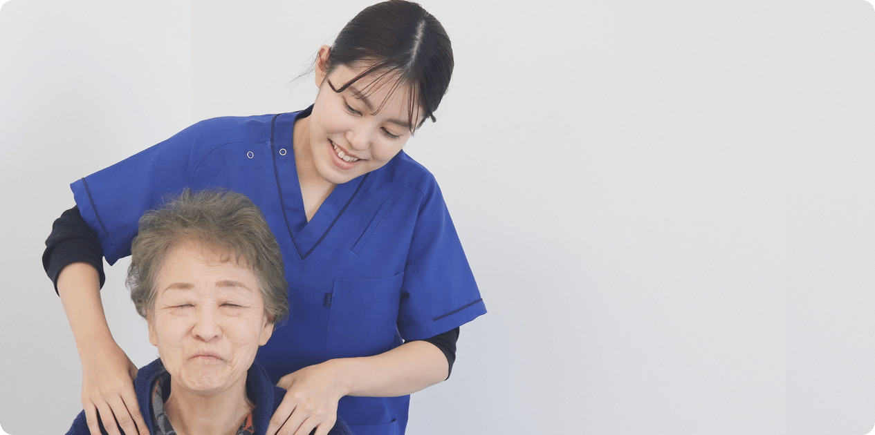 青い制服を着た介護・医療従事者が、高齢女性の肩に手を添えて笑顔で接している