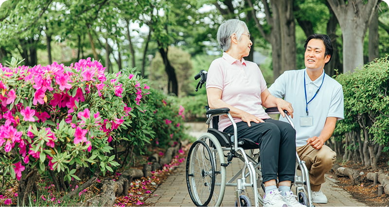 車椅子に座った高齢の女性が、介護士と楽しそうに会話をしている